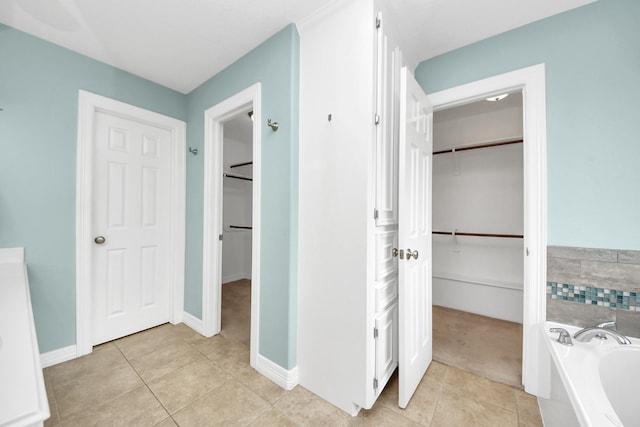 full bathroom featuring tile patterned floors, a spacious closet, baseboards, and a garden tub