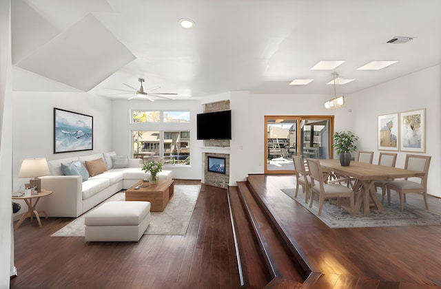 living room featuring visible vents, ceiling fan, hardwood / wood-style floors, a skylight, and a glass covered fireplace