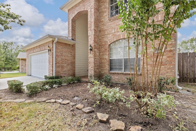 view of side of home with brick siding, concrete driveway, a garage, and fence