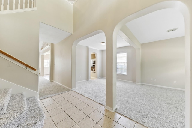 interior space featuring visible vents, baseboards, light carpet, light tile patterned floors, and arched walkways