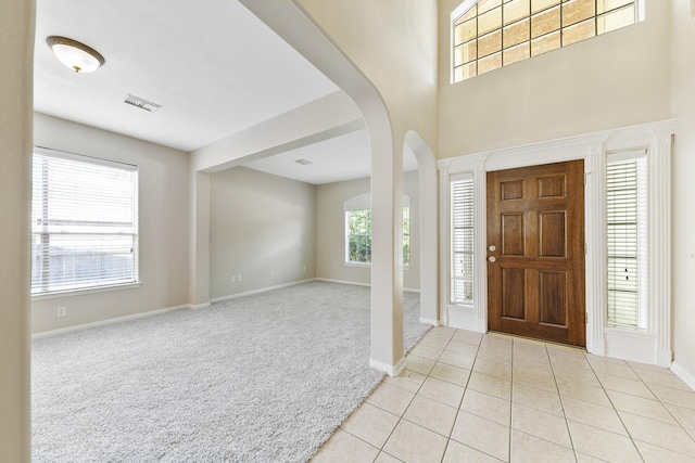 carpeted entrance foyer with tile patterned flooring, arched walkways, visible vents, and baseboards