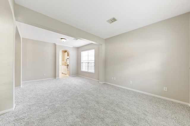 carpeted empty room with visible vents, arched walkways, and baseboards