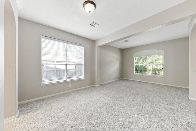 carpeted spare room with plenty of natural light, visible vents, baseboards, and arched walkways