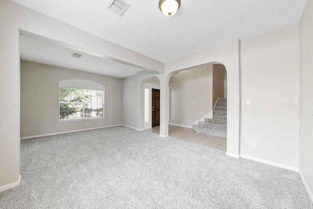 carpeted empty room featuring visible vents, arched walkways, baseboards, and stairs