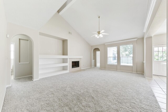 unfurnished living room with built in shelves, light colored carpet, a fireplace, arched walkways, and a ceiling fan