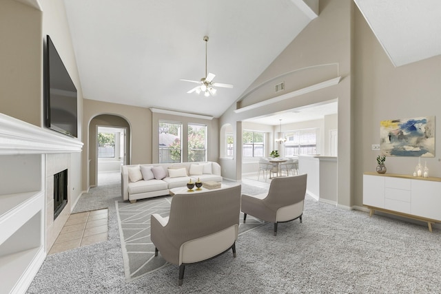 living area featuring visible vents, light colored carpet, ceiling fan with notable chandelier, a fireplace, and high vaulted ceiling