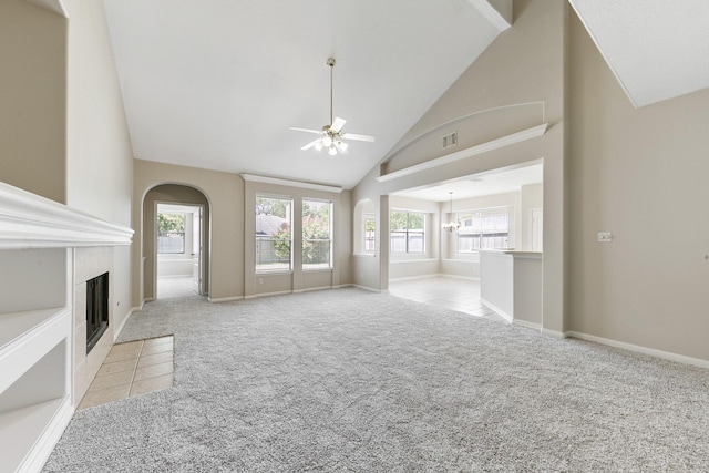 unfurnished living room with high vaulted ceiling, a tiled fireplace, ceiling fan with notable chandelier, arched walkways, and light colored carpet