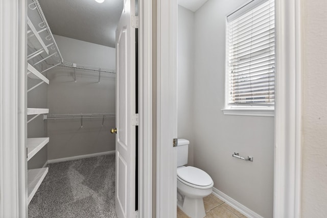 bathroom with a spacious closet, toilet, and baseboards