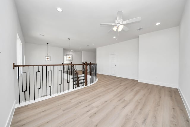 spare room featuring recessed lighting, light wood-type flooring, baseboards, and ceiling fan with notable chandelier