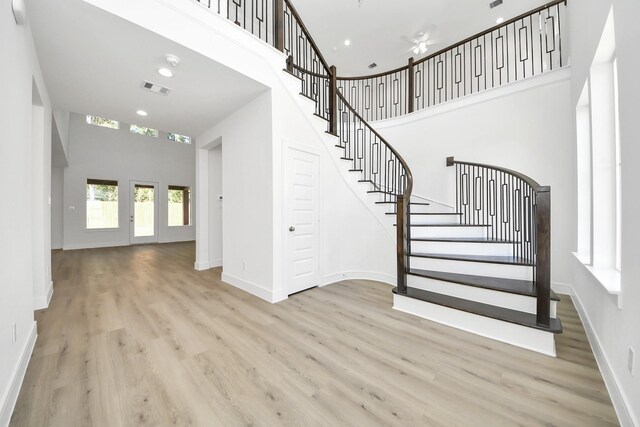 stairway with a high ceiling, wood finished floors, visible vents, and baseboards