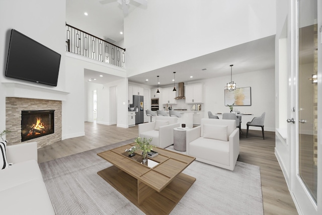 living room with a tiled fireplace, light wood-style flooring, recessed lighting, and a high ceiling