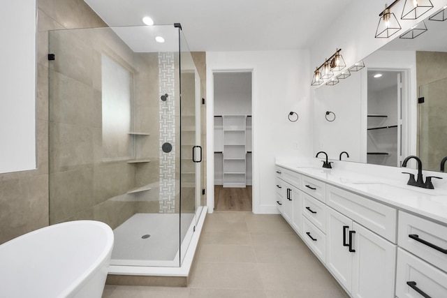 full bath with double vanity, a shower stall, a spacious closet, and a sink