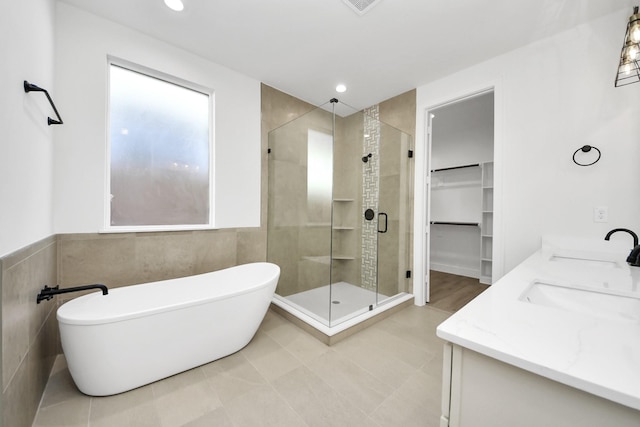 full bathroom featuring a freestanding tub, recessed lighting, a sink, a shower stall, and tile walls