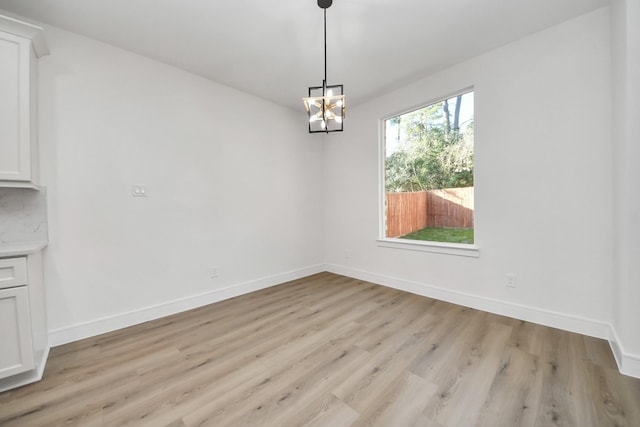 unfurnished dining area featuring a notable chandelier, light wood-type flooring, and baseboards