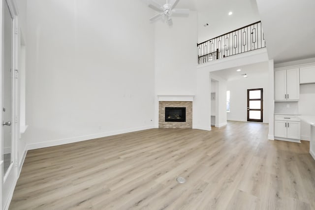 unfurnished living room featuring a fireplace, baseboards, light wood-type flooring, and a ceiling fan