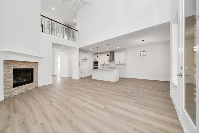 unfurnished living room with recessed lighting, light wood-type flooring, baseboards, and a glass covered fireplace