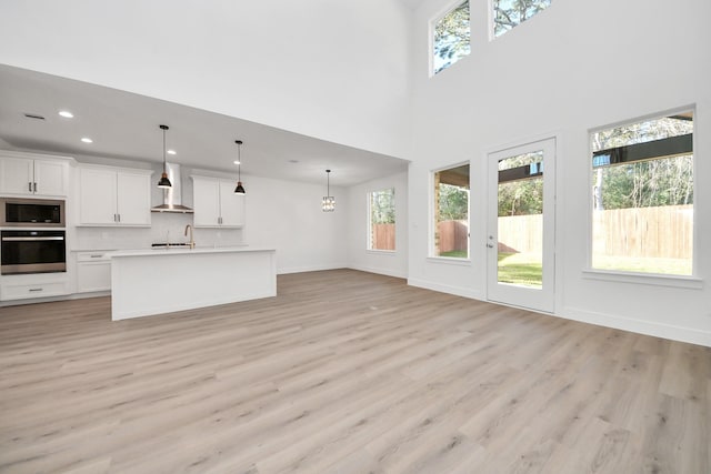 unfurnished living room with light wood finished floors, baseboards, a chandelier, recessed lighting, and a towering ceiling