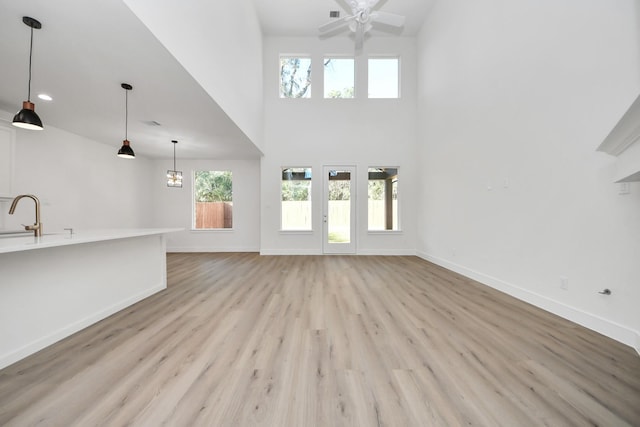 unfurnished living room with baseboards, light wood finished floors, a sink, ceiling fan, and a towering ceiling