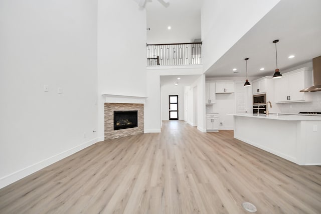 unfurnished living room with baseboards, a fireplace, recessed lighting, a towering ceiling, and light wood-type flooring