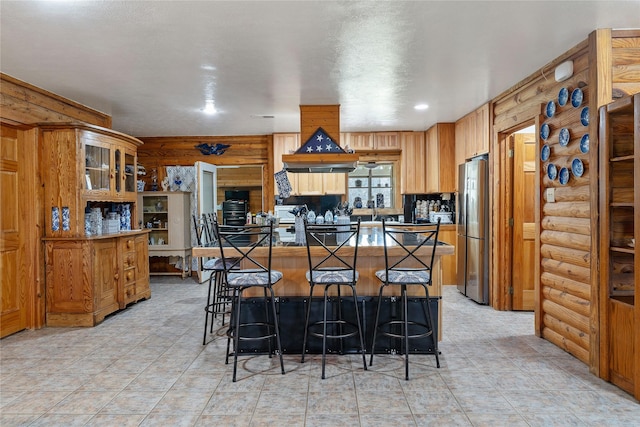 kitchen with a kitchen bar, dark countertops, freestanding refrigerator, log walls, and glass insert cabinets