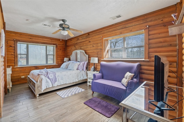 bedroom featuring visible vents, a textured ceiling, log walls, and wood finished floors