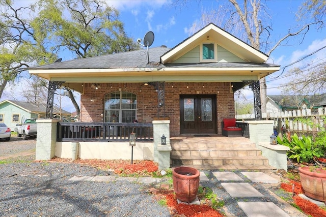 view of front of house featuring brick siding, covered porch, a shingled roof, and fence