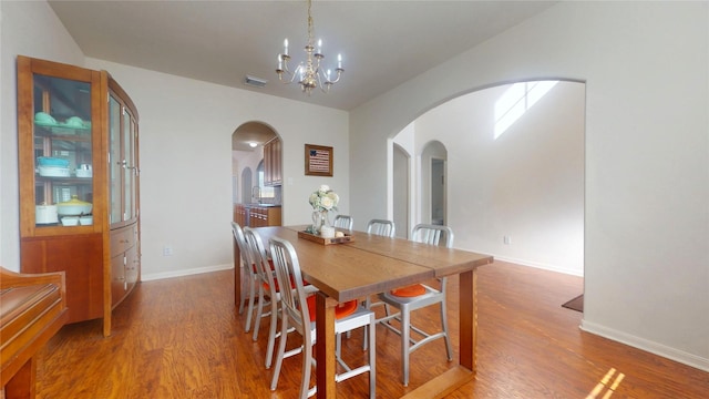 dining area featuring visible vents, arched walkways, a notable chandelier, and wood finished floors