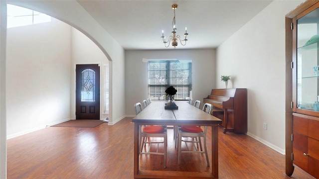 dining space with baseboards, arched walkways, a notable chandelier, and wood finished floors