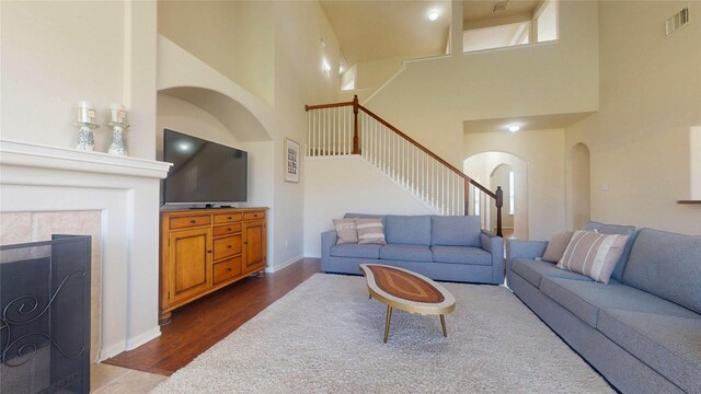 living room featuring stairway, visible vents, baseboards, arched walkways, and dark wood-type flooring