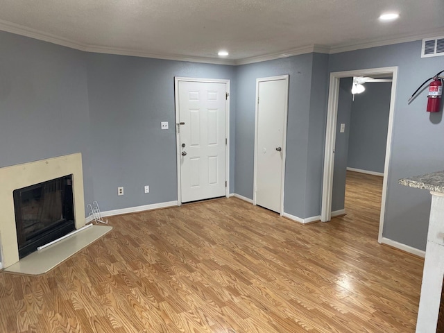 unfurnished living room with baseboards, visible vents, light wood-style flooring, a fireplace with raised hearth, and ornamental molding