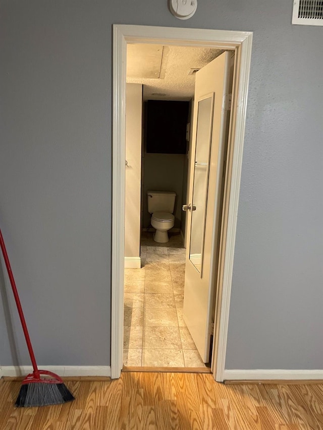 hall featuring visible vents, light wood-style flooring, a textured ceiling, and baseboards