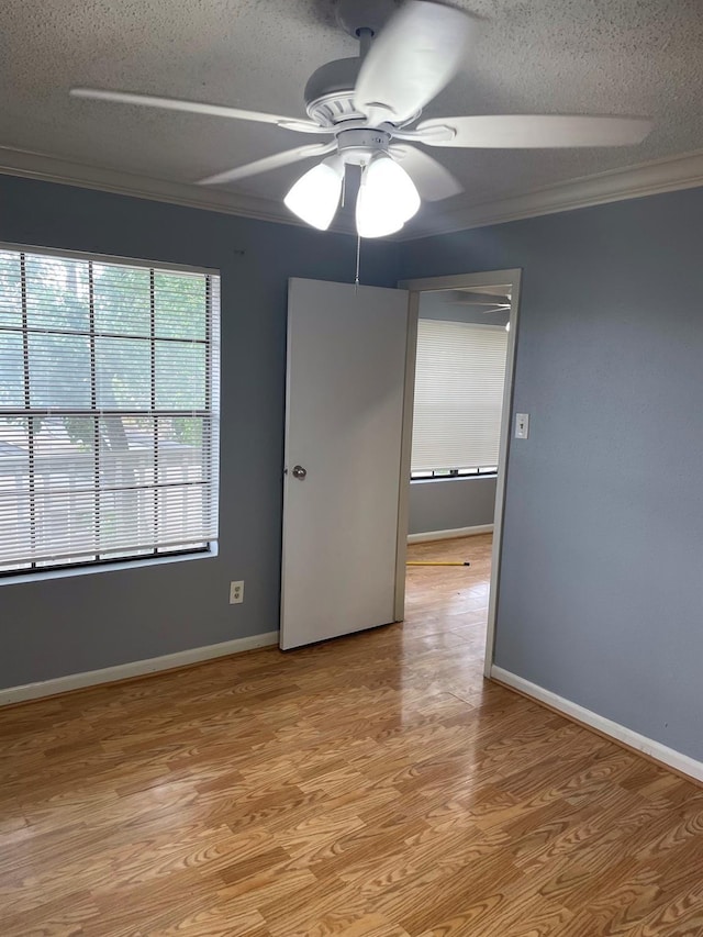 spare room with baseboards, ceiling fan, a textured ceiling, crown molding, and light wood-type flooring