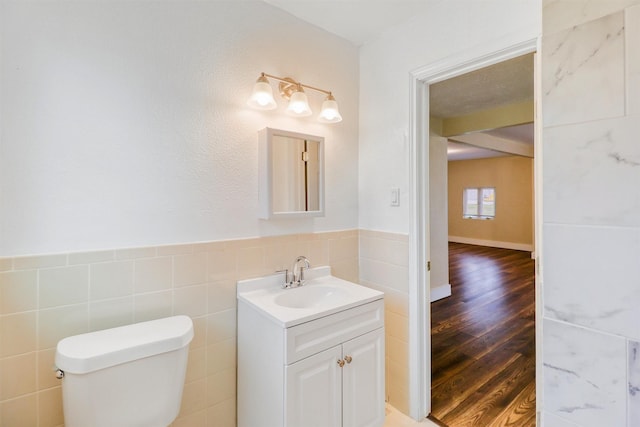 half bathroom with vanity, wood finished floors, wainscoting, tile walls, and toilet