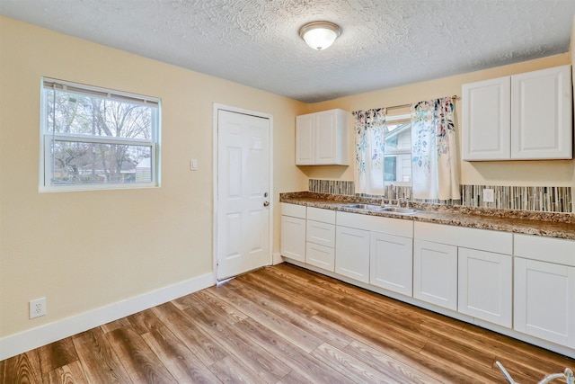 kitchen with a sink, a textured ceiling, white cabinetry, light wood finished floors, and baseboards