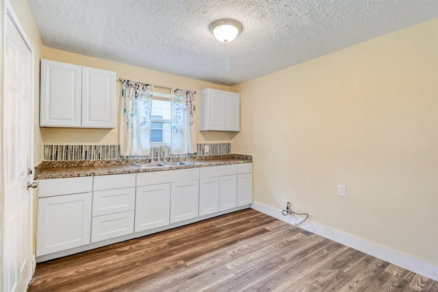 kitchen featuring white cabinetry, baseboards, wood finished floors, a textured ceiling, and a sink