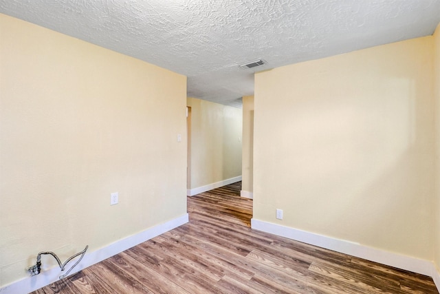 unfurnished room featuring visible vents, baseboards, a textured ceiling, and wood finished floors