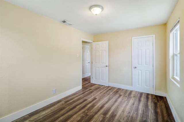 unfurnished bedroom featuring visible vents, multiple windows, baseboards, and dark wood-style flooring