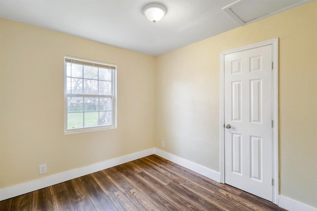 unfurnished room with baseboards, attic access, and dark wood-style flooring