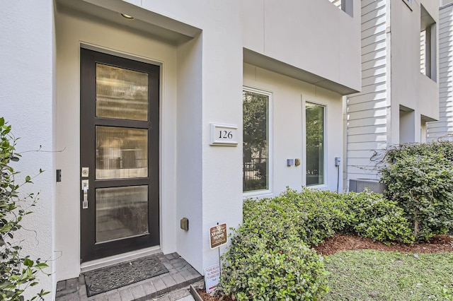 doorway to property featuring stucco siding and cooling unit