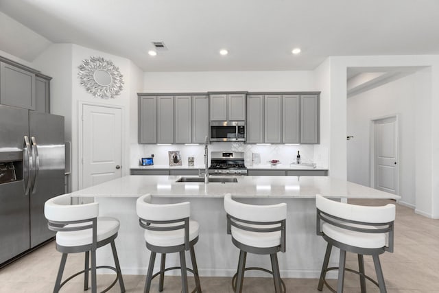 kitchen featuring backsplash, gray cabinets, appliances with stainless steel finishes, and a kitchen island with sink