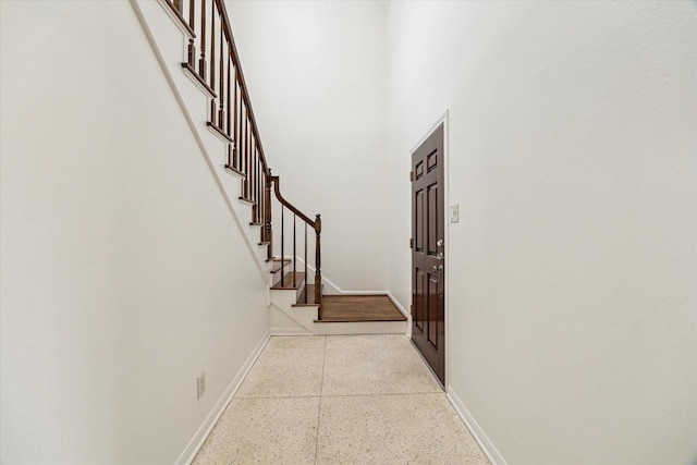 hallway featuring stairs, baseboards, speckled floor, and a towering ceiling