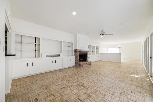 unfurnished living room featuring recessed lighting, a brick fireplace, and ceiling fan with notable chandelier