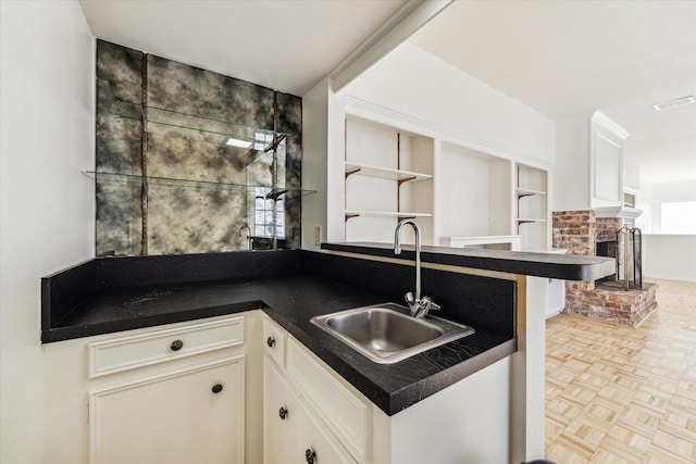 kitchen featuring visible vents, a sink, dark countertops, white cabinetry, and a brick fireplace