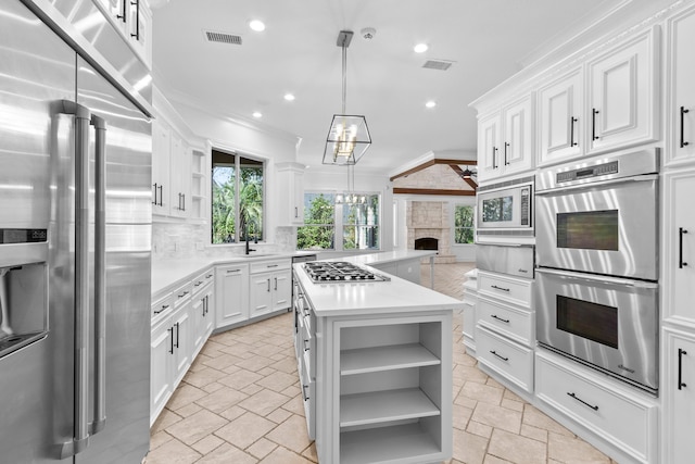 kitchen featuring stone tile floors, open shelves, appliances with stainless steel finishes, crown molding, and a chandelier