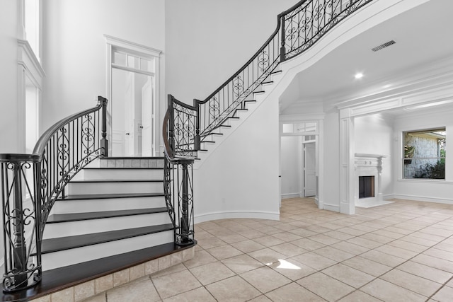 stairway featuring visible vents, ornamental molding, a high ceiling, a fireplace, and baseboards