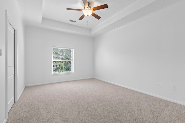 carpeted spare room featuring a tray ceiling, a ceiling fan, visible vents, and baseboards