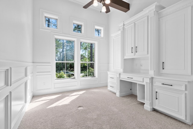 office space with light carpet, a decorative wall, built in desk, and a ceiling fan