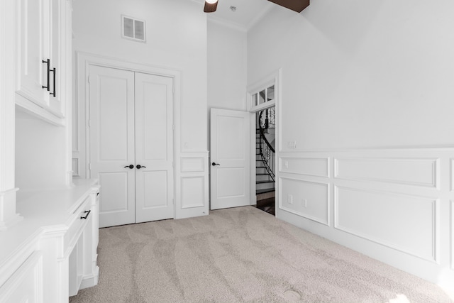 unfurnished bedroom featuring visible vents, light carpet, a closet, crown molding, and a decorative wall