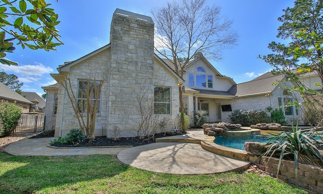 rear view of house featuring stone siding, a patio, fence, roof with shingles, and a chimney