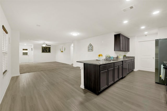 kitchen featuring visible vents, dark brown cabinetry, light wood-style flooring, dark stone countertops, and a sink